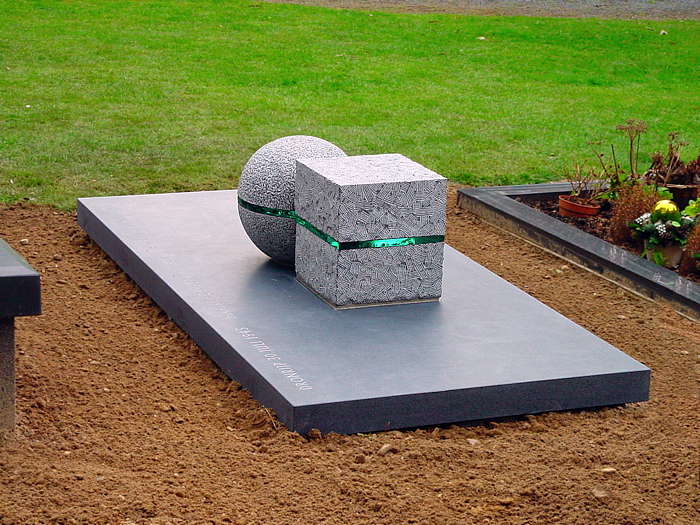 grafsteen van matte graniet (gezoet) waarop kubus en bol van gebouchardeerde hardsteen met glas daartussen verlijmd