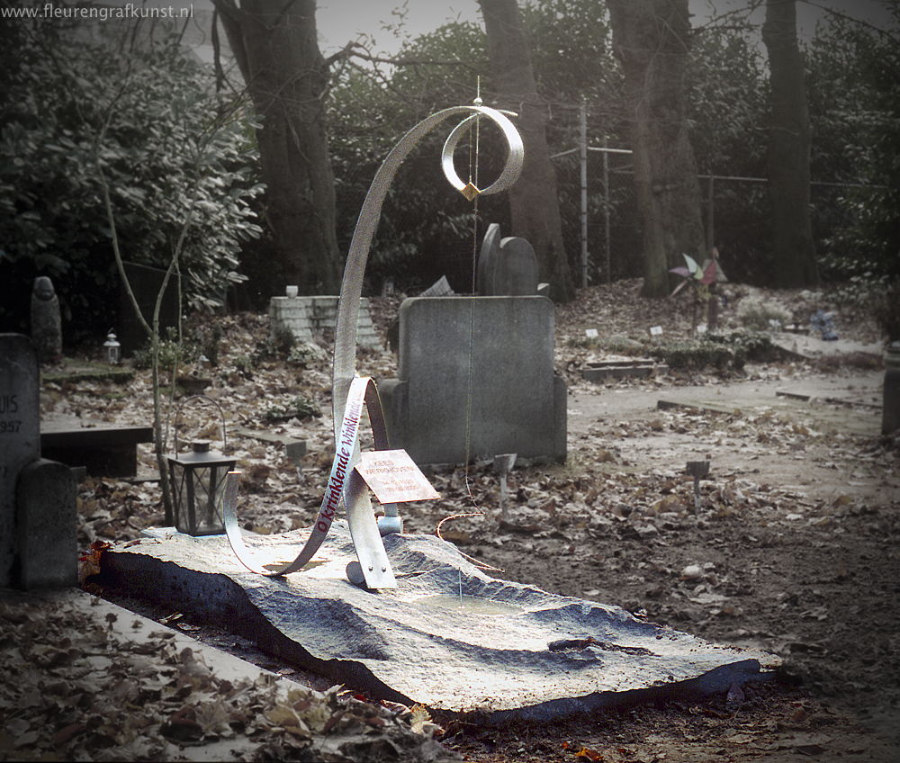 Grafmonument met grote krul van roest-vast-staal (RVS) en ruwe graniet. Een dunne pin roert zachtjes kringen in het water van begraafplaats Vredehof in Tilburg met een krinkelend en tinkelend geluid van het bronzen klankorgel