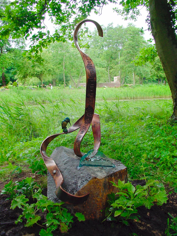 Urngrafmonument van basalt met letters op een tekst-guirlande van roodkoper en bronzen ijsvogel (begraafplaats bij crematorium Velsen)