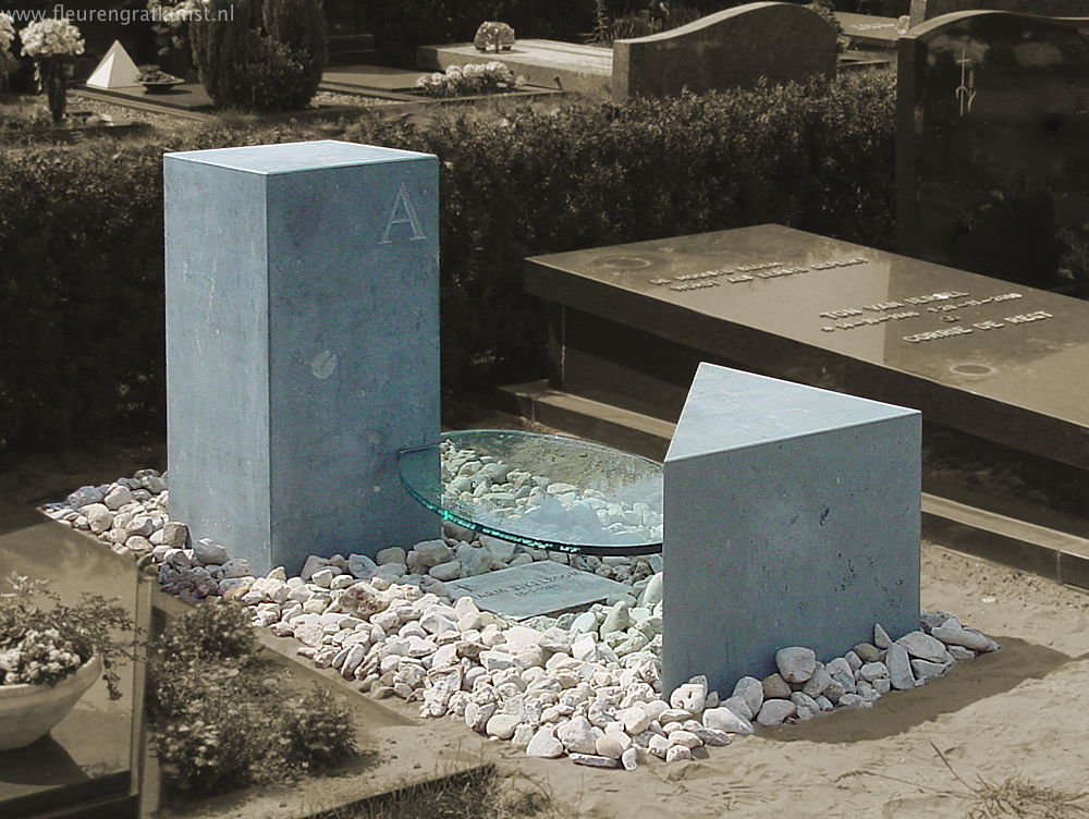 ovalen glasplaat met naam en datatekst is geklemd tussen twee blokken natuursteen op een graf in Oosterhout