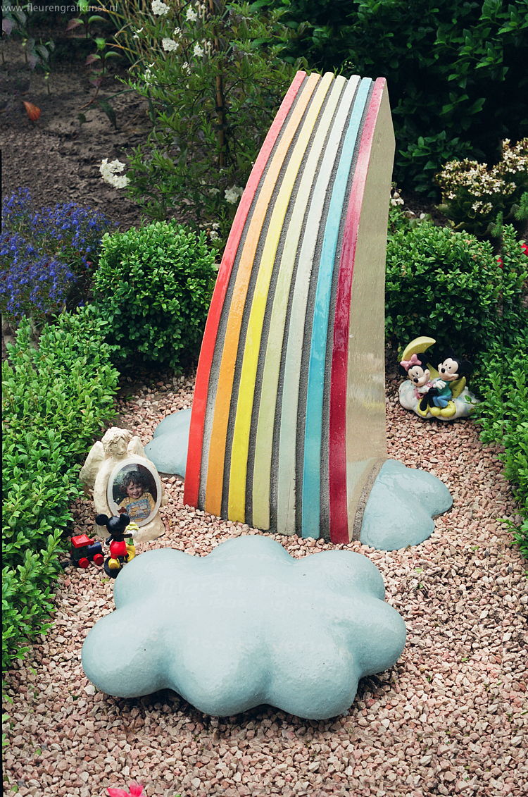 Gekleurde regenboog van keramiek met blauwe wolken voor een klein kindje (graf in Oisterwijk)